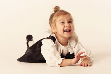 Naklejka premium cute little blond baby girl in black dress laughing lay on floor