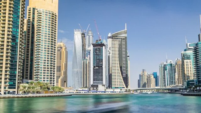 Dubai Marina canal with yachts and modern towers reflected in green water from waterfront in Dubai timelapse hyperlapse, United Arab Emirates. District with artificial canal