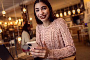 Portrait of young woman using smartphone in coffee shop.