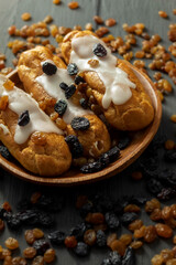 In a wooden plate are three eclairs with white icing and cream filling