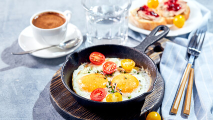 Fried eggs. Fried eggs from two eggs in cast-iron pan with cherry tomatoes and microgreens, toast and cup of coffee. Sunny morning breakfast concept
