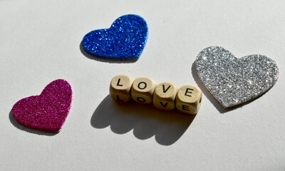 Four wooden cubes with letters, the word love is made up and three shiny hearts