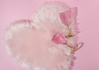 Rose champagne glasses on pastel pink faux fur heart. Romantic Valentine's day background. Minimal creative idea. 80s, 90s retro aesthetic fashion love drink concept.