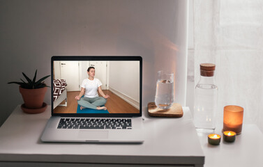 Online meditation, a screen with video call, woman doing yoga from home teaching sport online. White table with water
