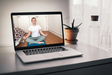 Online meditation, a screen with video call, woman doing yoga from home teaching sport online. White table with water
