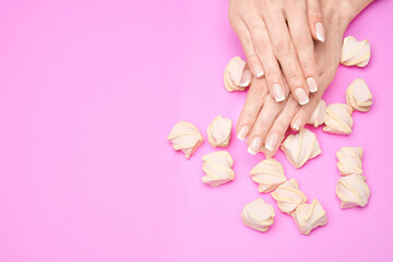 Obraz na płótnie Canvas Beautiful Female Hands with French manicure and marshmallows over colorful pink paper background