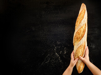 Children's hands holding a baguette on a black background.