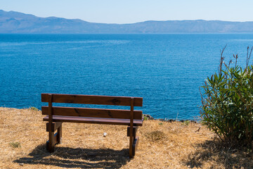 Naklejka na ściany i meble Empty wooden bench, on edge of grassy cliff, facing the ocean. Travel magazine cover concept