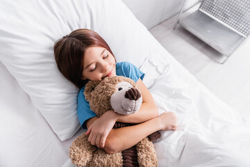 top view of happy girl sleeping with teddy bear in hospital bed