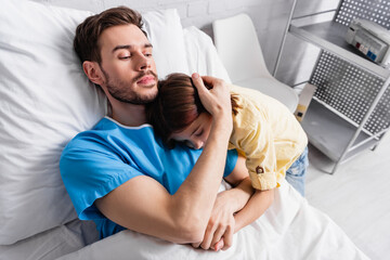Fototapeta premium ill man embracing daughter while lying in hospital bed