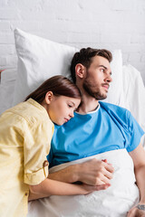 Fototapeta premium girl leaning on father lying on hospital bed and holding his hand