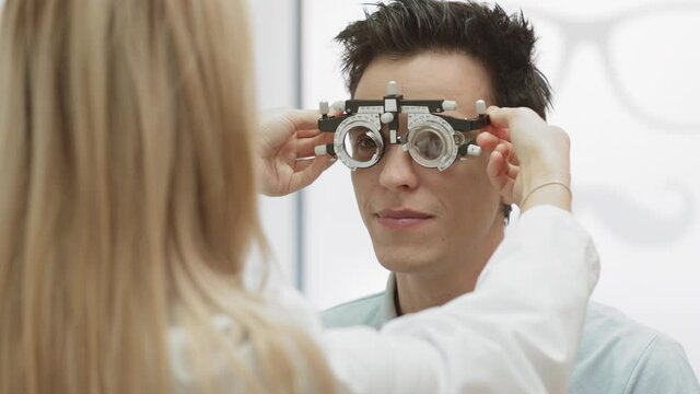 Over The Shoulder View Of Caucasian Female Ophthalmologist Examining Male Patient Eyesight By Putting Special Ophthalmological Tool On Him