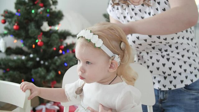 Concept of hearing impairment and their treatment. Young Mother connect a cochlear implants to her daughter's head