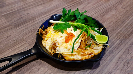 Fried noodle in Thai style with prawns and vegetable in hot pan on wooden background or table at Restaurant. Asian people call this food Pad Thai and Famous in Thailand. Delicious meal