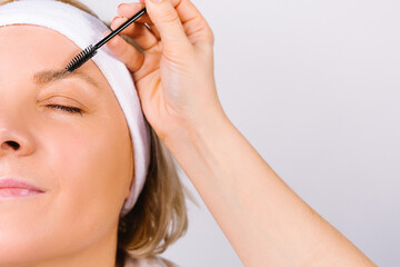 Enlarged photo where the hand of the master makes the lamination of the eyebrows of a woman with a bandage on her head. Fashion trends on a white background.
