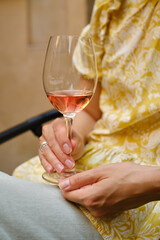 A glass of rose wine in the hands of a girl relaxing on restaurant terrace. Summer holiday. Celebrate and enjoy moment. Alcoholic drink tasting. Romantic evening aperitif. Wine glass closeup