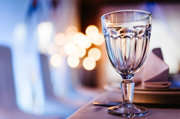 Close up picture of empty glasses in restaurant and cutlery. Silverware or flatware on plates and wine glasses. Reflection, bokeh and bright light.