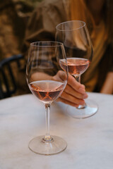 A glass of rose wine in the hands of a girl relaxing on restaurant terrace. Summer holiday. Celebrate and enjoy moment. Alcoholic drink tasting. Romantic evening aperitif. Wine glass closeup