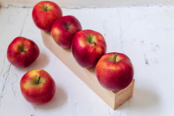 Six red apples on a white background, four of them lying on a wooden stand