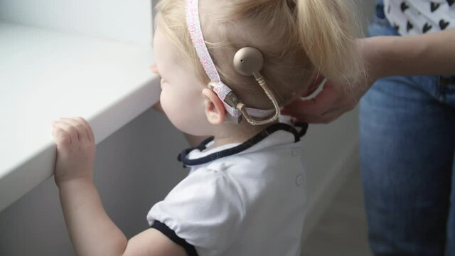 Concept of hearing impairment and their treatment. Young Mother connect a cochlear implants to her daughter's head