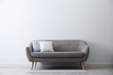 Grey sofa with pillows near white wall in stylish living room interior. Space for text