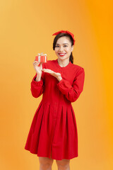 people, christmas, birthday and holidays concept - happy young woman in red dress showing/holding with gift box over orange background.