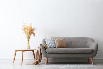 Grey sofa with pillows near white wall in stylish living room interior - obrazy, fototapety, plakaty