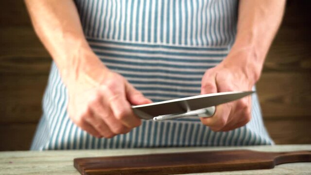 A male chef in an apron is sharpening a knife with a sharpener before cooking