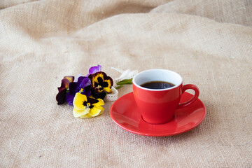 パンジーの花束と赤いコーヒーカップにいれたコーヒー（麻布の背景）