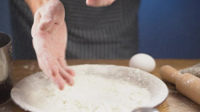 Male cook is making claps to shake the flour off his hands. Concept of the cooking process of baking or other dough products
