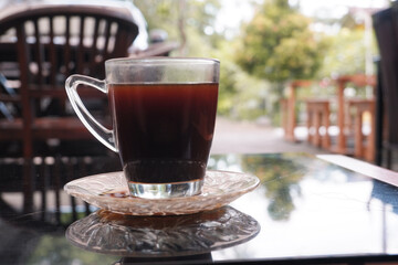 A glass of black coffee on a glass table with a blurred background 