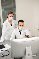 group of two medical professional male and female doctor wearing surgical mask in a hospital office desk with computer