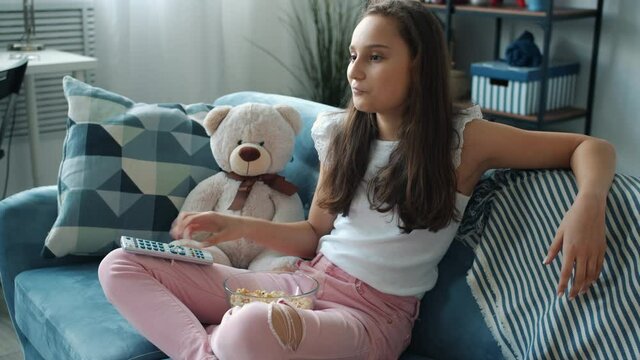 Happy kid is watching funny comedy on TV eating popcorn and laughing having fun alone in apartment. Stay home activities and television concept.