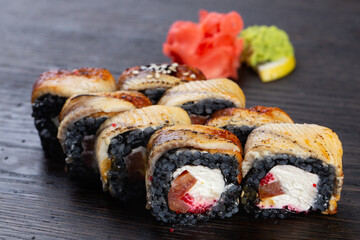 traditional black Japanese sushi with tuna and soft cheese, cucumber and red caviar, garnished with sauce and white sesame seeds. Japanese kitchen. Japanese restaurant.