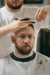Obraz na płótnie Canvas Close up master barber, stylist does the hairstyle to guy, young man. Professional occupation, male beauty concept. Cares of hair, mustache, beard of client. Soft colors and focus, vintage.