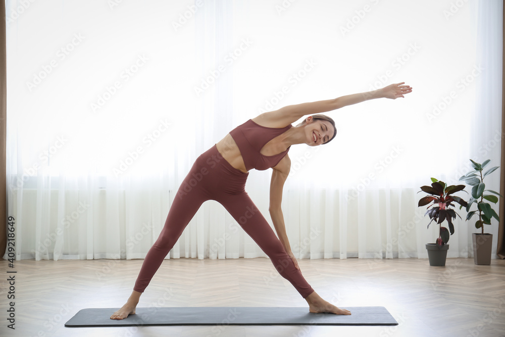 Sticker Young woman practicing triangle asana in yoga studio. Trikonasana pose