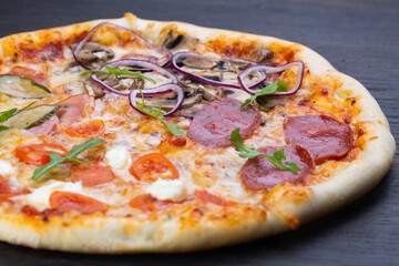 Delicious italian pizza with fresh tomatoes, olives, onions, sausage, ham and basil on an old wooden board