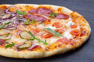 Delicious italian pizza with fresh tomatoes, olives, onions, sausage, ham and basil on an old wooden board