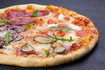 Delicious italian pizza with fresh tomatoes, olives, onions, sausage, ham and basil on an old wooden board
