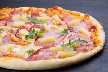 Delicious italian pizza with fresh tomatoes, pineapples, olives, ham and basil on an old wooden board