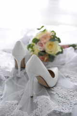 Pair of white high heel shoes, veil and wedding bouquet on light background