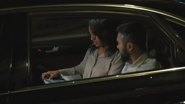 Tracking handheld footage of hard-working business partners doing paperwork at backseat of expensive black car at night