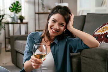 Happy woman sitting on the floor, drinking wine. Smiling woman celebrate with wine at home..