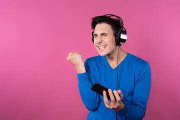 The young guy is playing the phone. Listen to music. Emotions and feelings. Pink background.