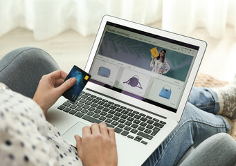 Woman with credit card using laptop for online shopping indoors, closeup