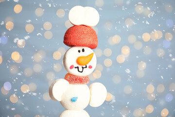 Funny snowman made of marshmallows against blurred festive lights, closeup. Space for text
