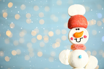 Funny snowman made of marshmallows against blurred festive lights, closeup. Space for text