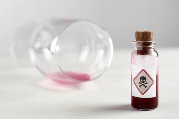 Vial of poison and partially emptied glass on light background