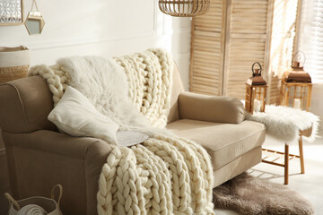 Cozy living room interior with beige sofa, knitted blanket and cushions