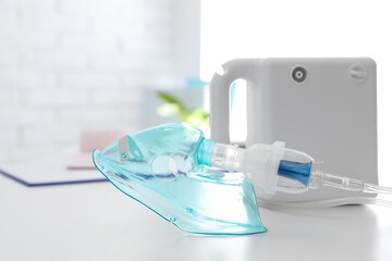 Modern nebulizer with face mask on white table indoors. Equipment for inhalation